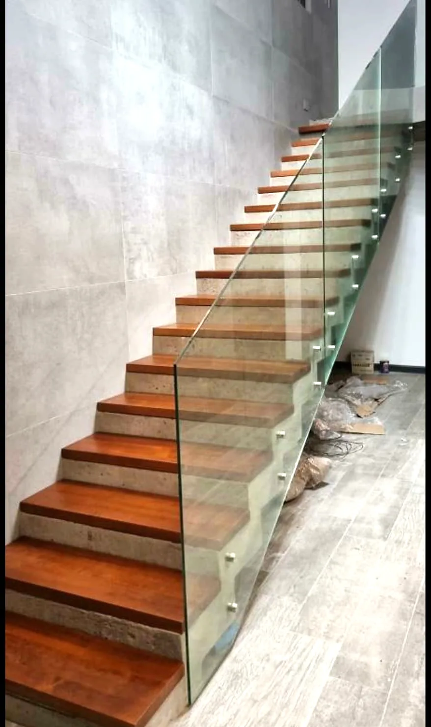Escalera con huellas de madera barnizada y baranda de vidrio en obra